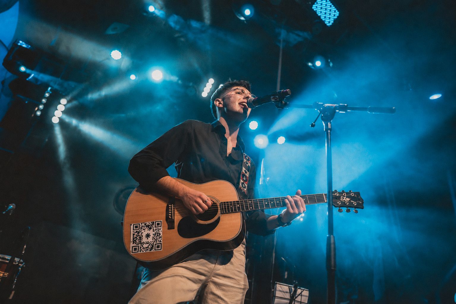 Giuliano performing with his guitar under blue stage lights