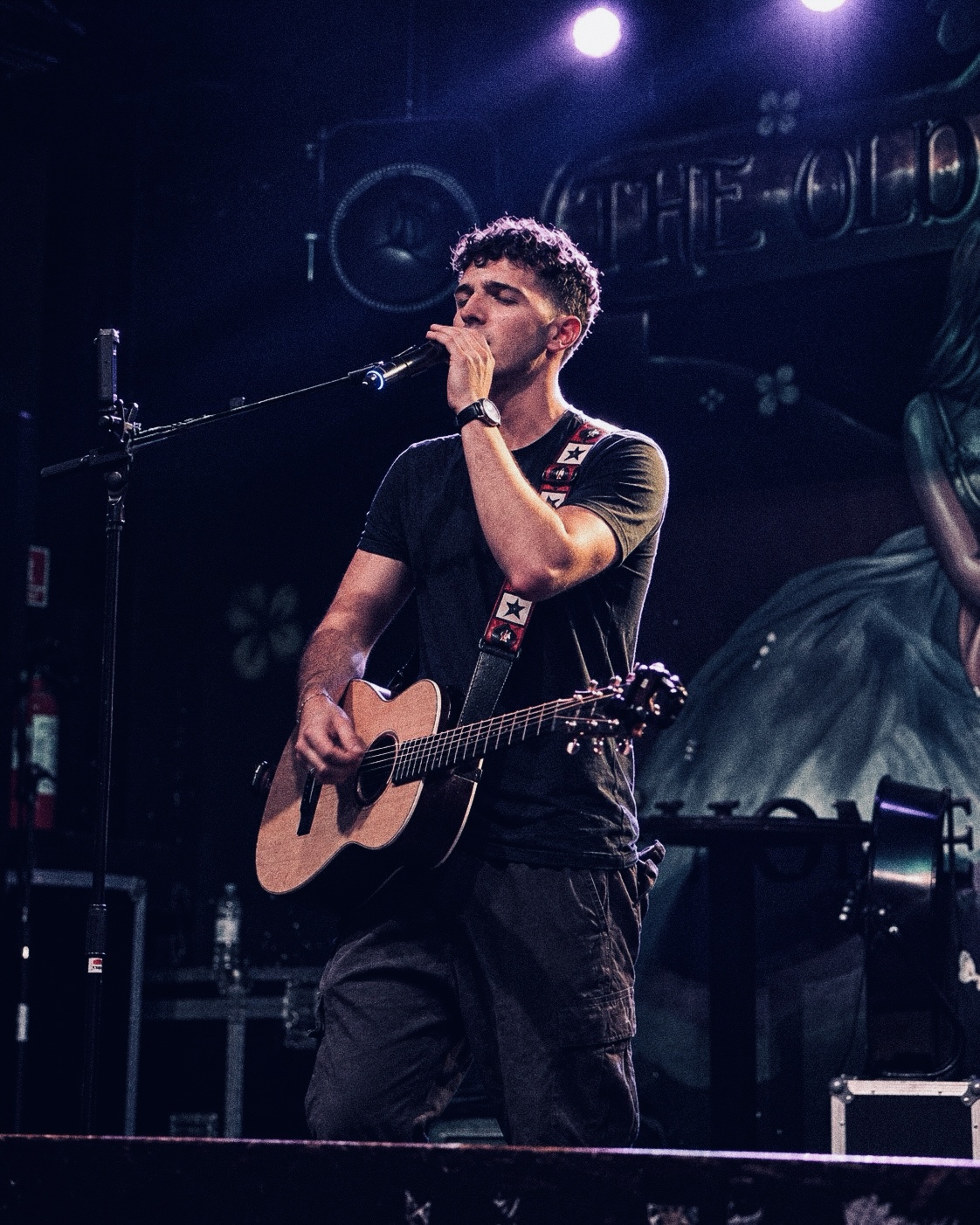 Giuliano singing with his acoustic guitar under purple stage lights