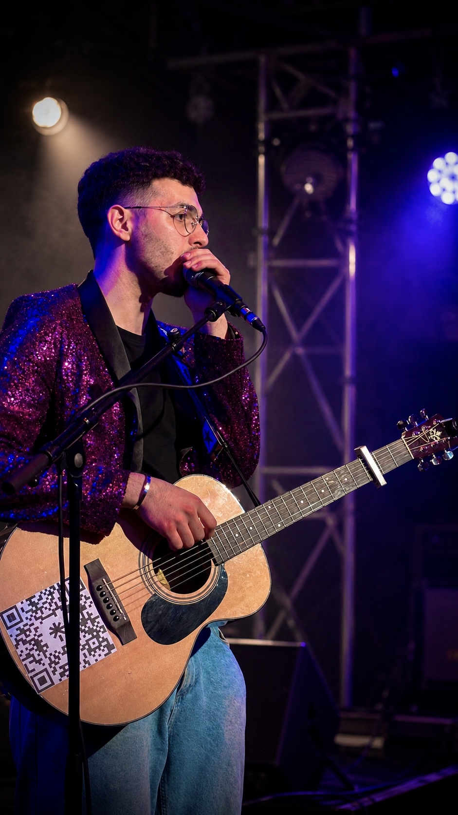 Giuliano with his guitar and microphone, wearing a purple jacket on stage