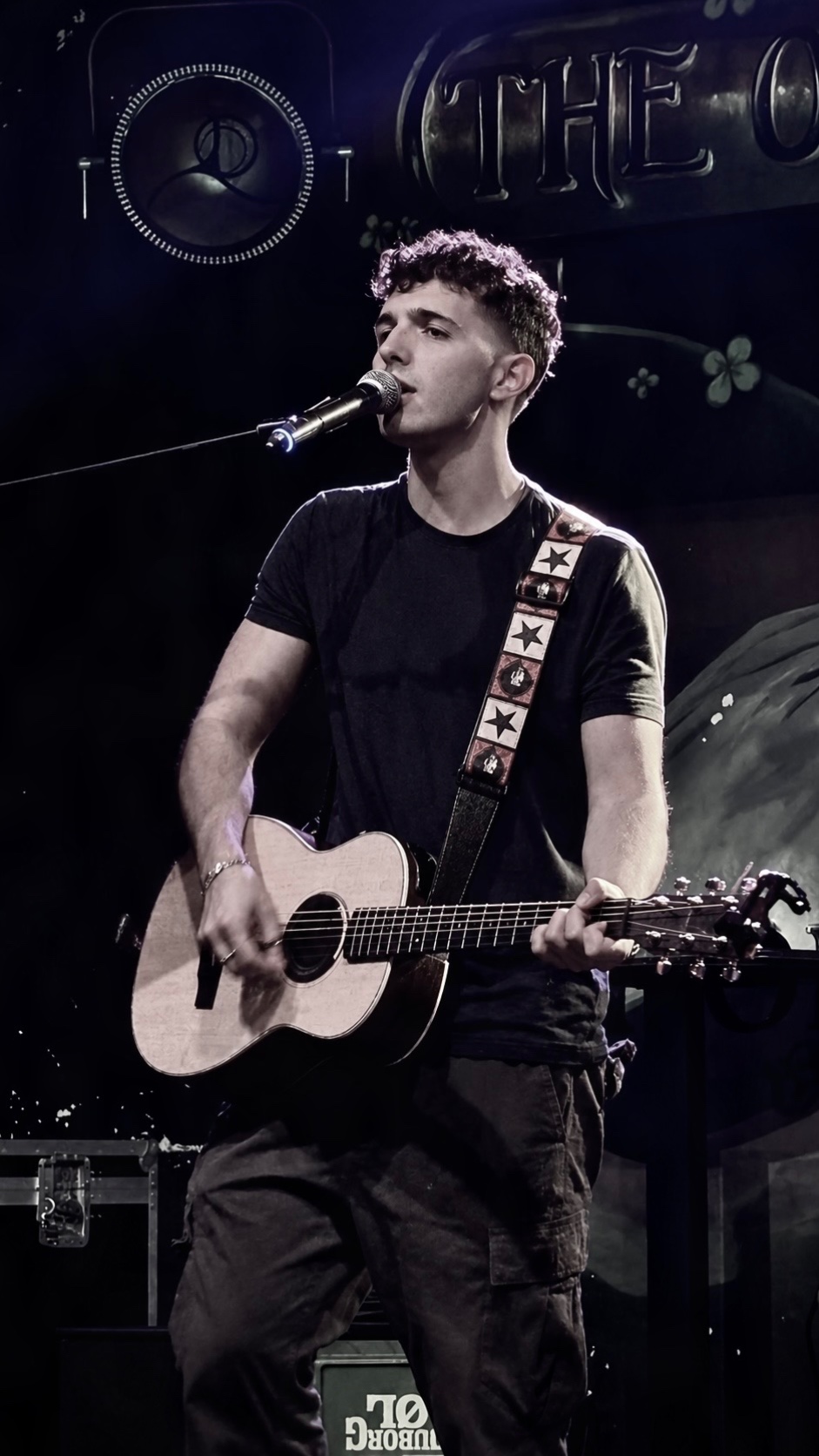 Giuliano singing and playing acoustic guitar in a sepia-toned photograph